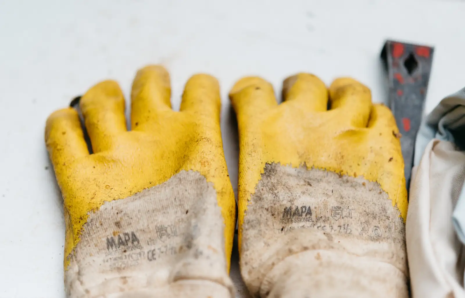 A pair of worn yellow work gloves on a white bench